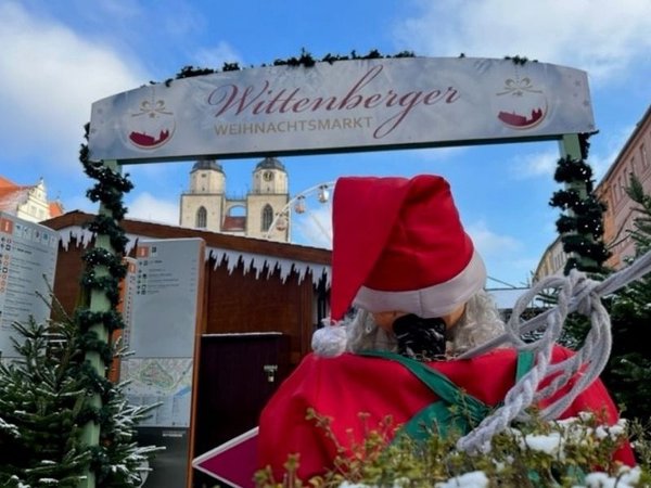 Eingang Holztorbogen zum Weihnachtsmarkt Lutherstadt Wittenberg über die Schulter eines Weihnachtsmann mit Blck auf Stadtkirche